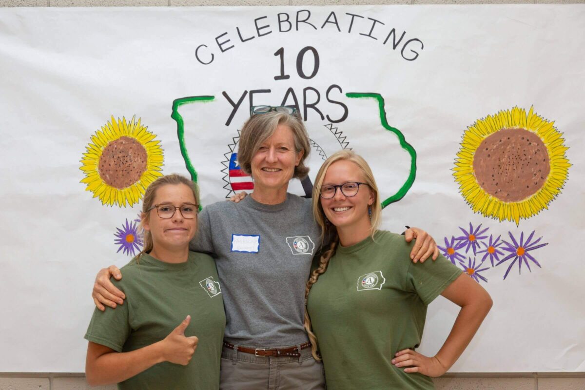 Three women stand in front of a banner that reads 