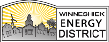 Logo for Winneshiek Energy District featuring a stylized town skyline with a wind turbine, sun rays, and bold text on a white and grey background.