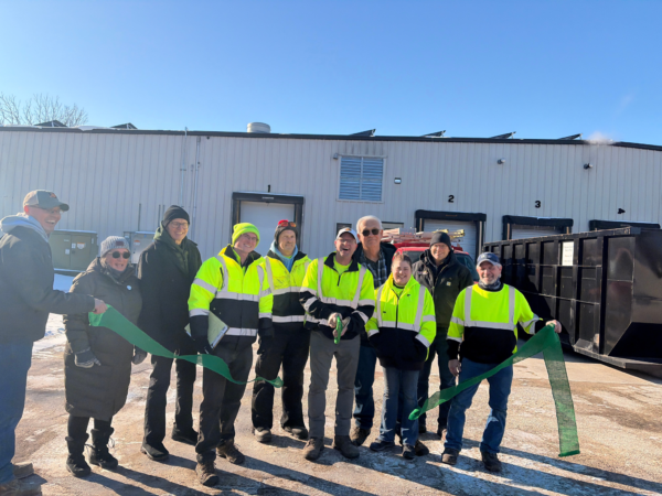 Recycling employees in high vis jackets hold and cut green ribbon
